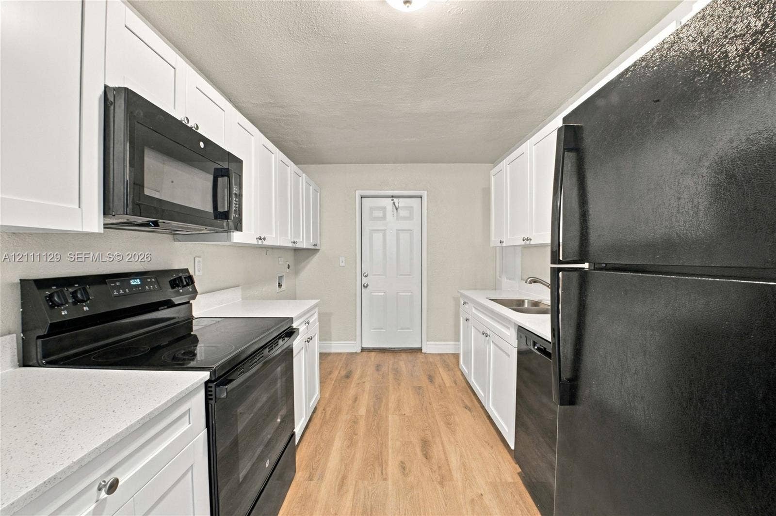 Kitchen featuring white shaker-style cabinetry, light-toned wood-finish flooring, solid surface countertops, and black built-in appliances