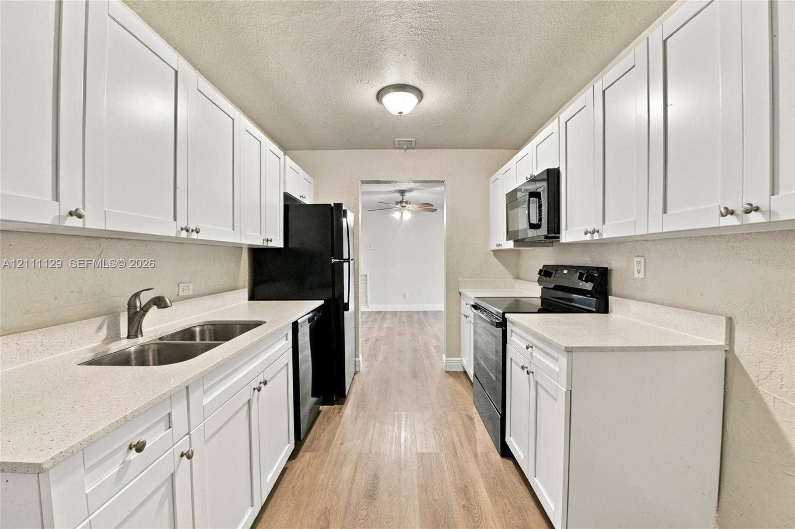 Kitchen featuring white shaker-style cabinetry, solid-surface countertops, dual-basin stainless steel sink, black appliances, and wood-finish flooring