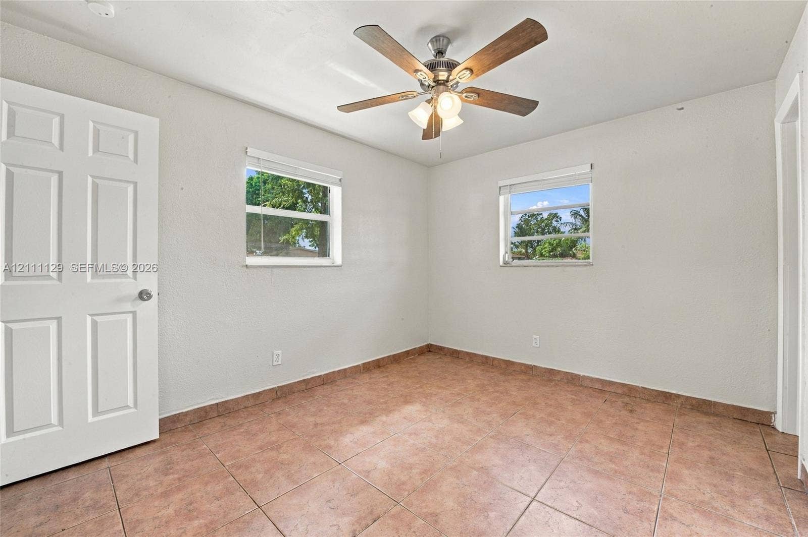 Interior space featuring tile flooring, a multi-blade ceiling fan with integrated lighting, dual windows, and a six-panel door