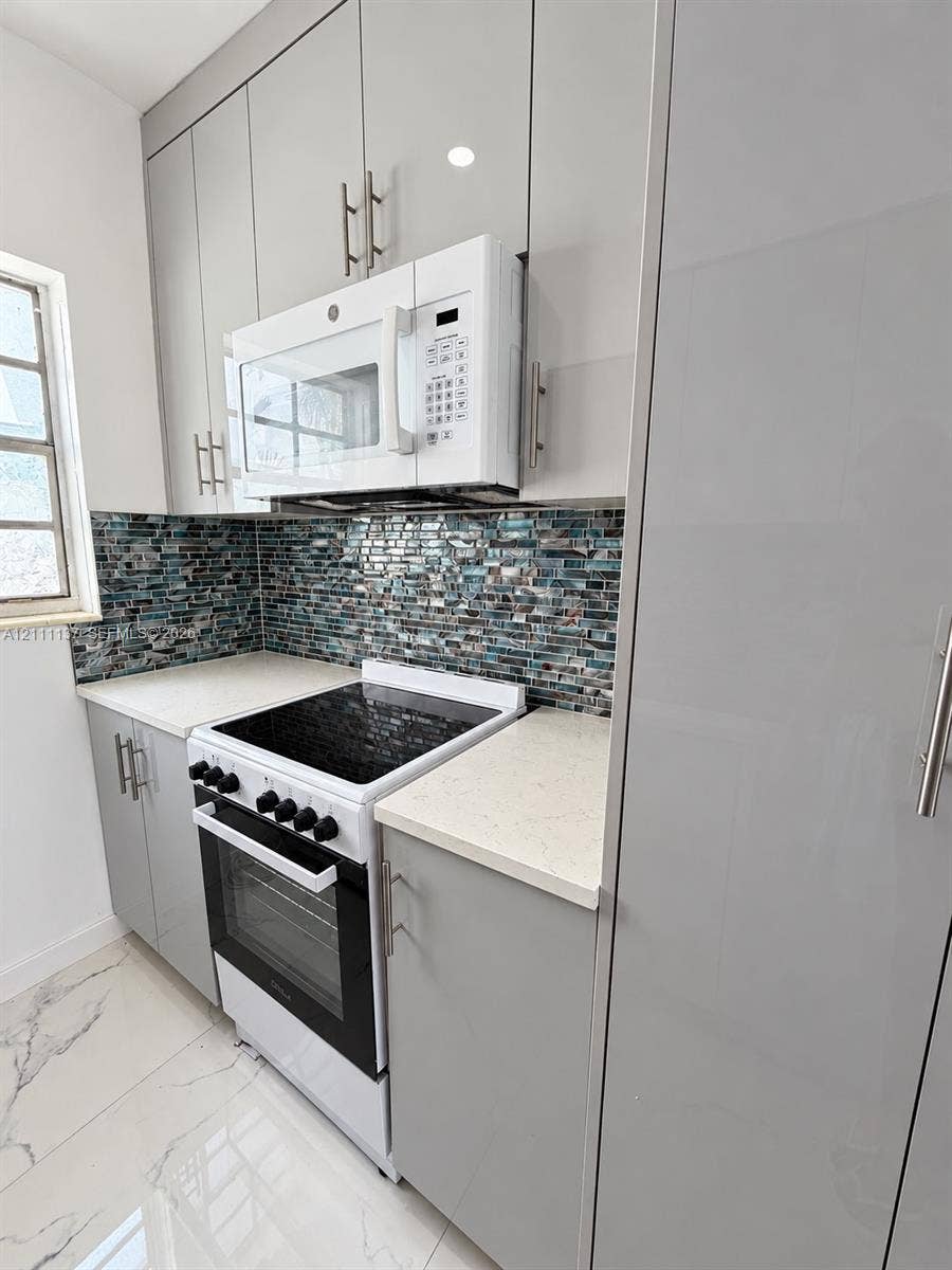 635 8th Street, #205, Miami Beach, Miami Beach, FL 33139 Modern kitchen featuring gloss-finish cabinetry, stone-style countertops, mosaic tile backsplash, stainless steel hardware, and large-format tile flooring