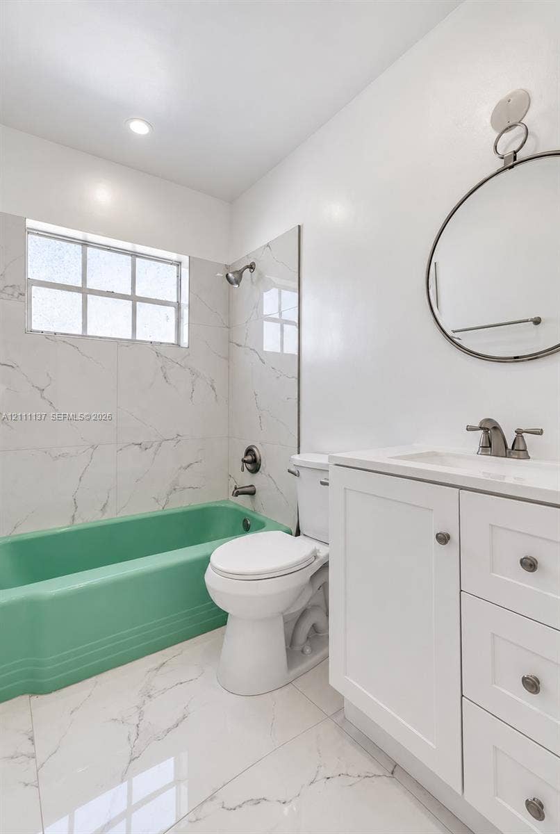 635 8th Street, #205, Miami Beach, Miami Beach, FL 33139 Bathroom featuring white tile flooring and wall surrounds with grey veining, a colored soaking tub, a white vanity cabinet with a stone-finish countertop, and a circular wall-mounted mirror