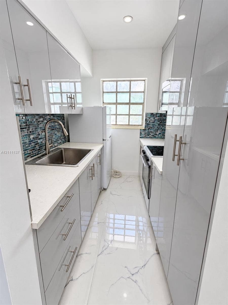 635 8th Street, #205, Miami Beach, Miami Beach, FL 33139 Kitchen featuring high-gloss cabinetry, stone-surface countertops, blue mosaic tile backsplash, stainless steel sink with gooseneck faucet, and large-format porcelain tile flooring