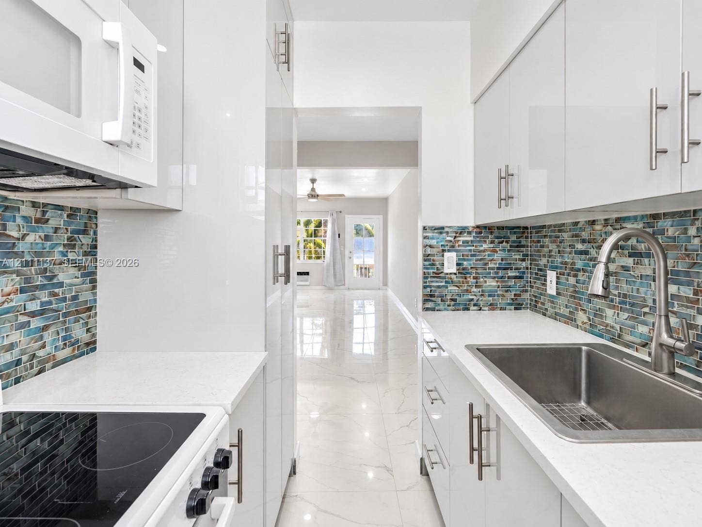 635 8th Street, #205, Miami Beach, Miami Beach, FL 33139 Kitchen featuring high-gloss white cabinetry, white quartz countertops, multi-tonal glass tile backsplash, stainless steel undermount sink with arched pull-down faucet, and polished stone-finish flooring