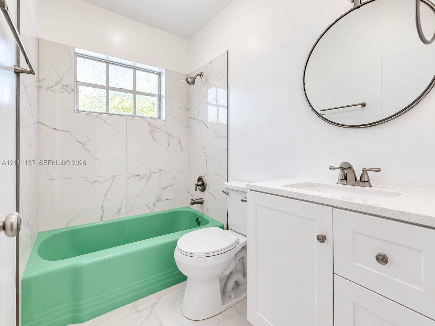 635 8th Street, #205, Miami Beach, Miami Beach, FL 33139 Bathroom featuring a white vanity with a composite countertop, oval wall-mounted mirror, large-format tile tub surround, and a colored bathtub