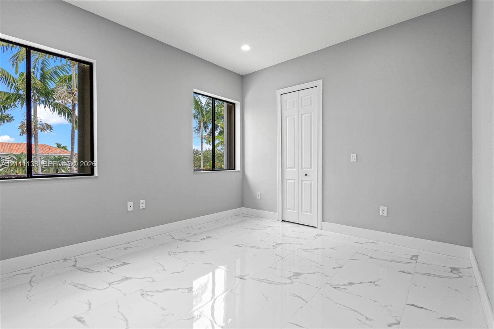 19363 SW 79th Avenue, Cutler Bay, FL 33157 Interior room featuring large-format stone-look flooring, neutral grey walls, dual windows with dark frames, and a white bifold closet door