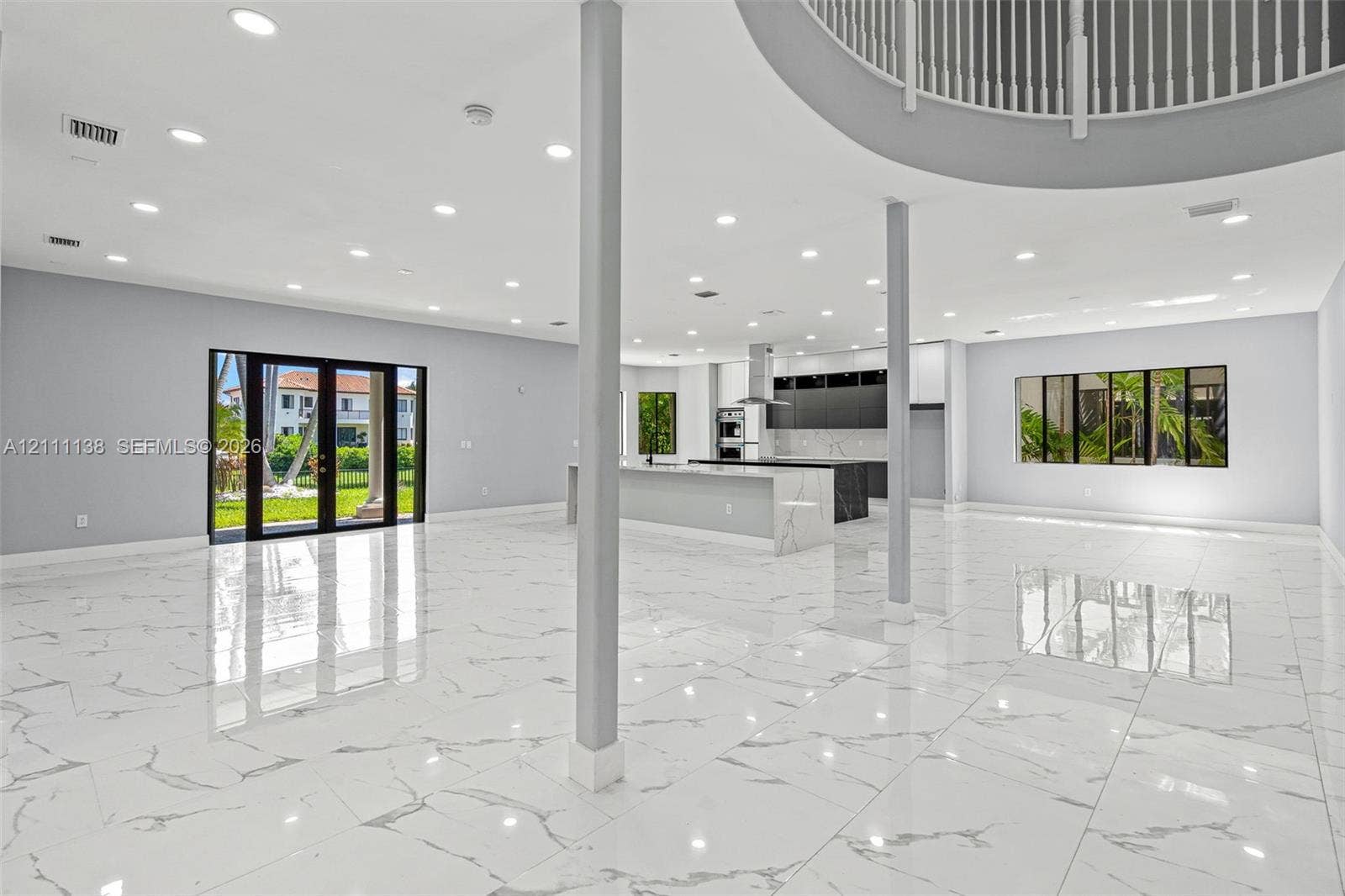 19363 SW 79th Avenue, Cutler Bay, FL 33157 Open-concept interior featuring large-format stone-finish flooring, recessed lighting, a kitchen island with stone-finish countertop, structural support columns, and a mezzanine balcony with a metal railing