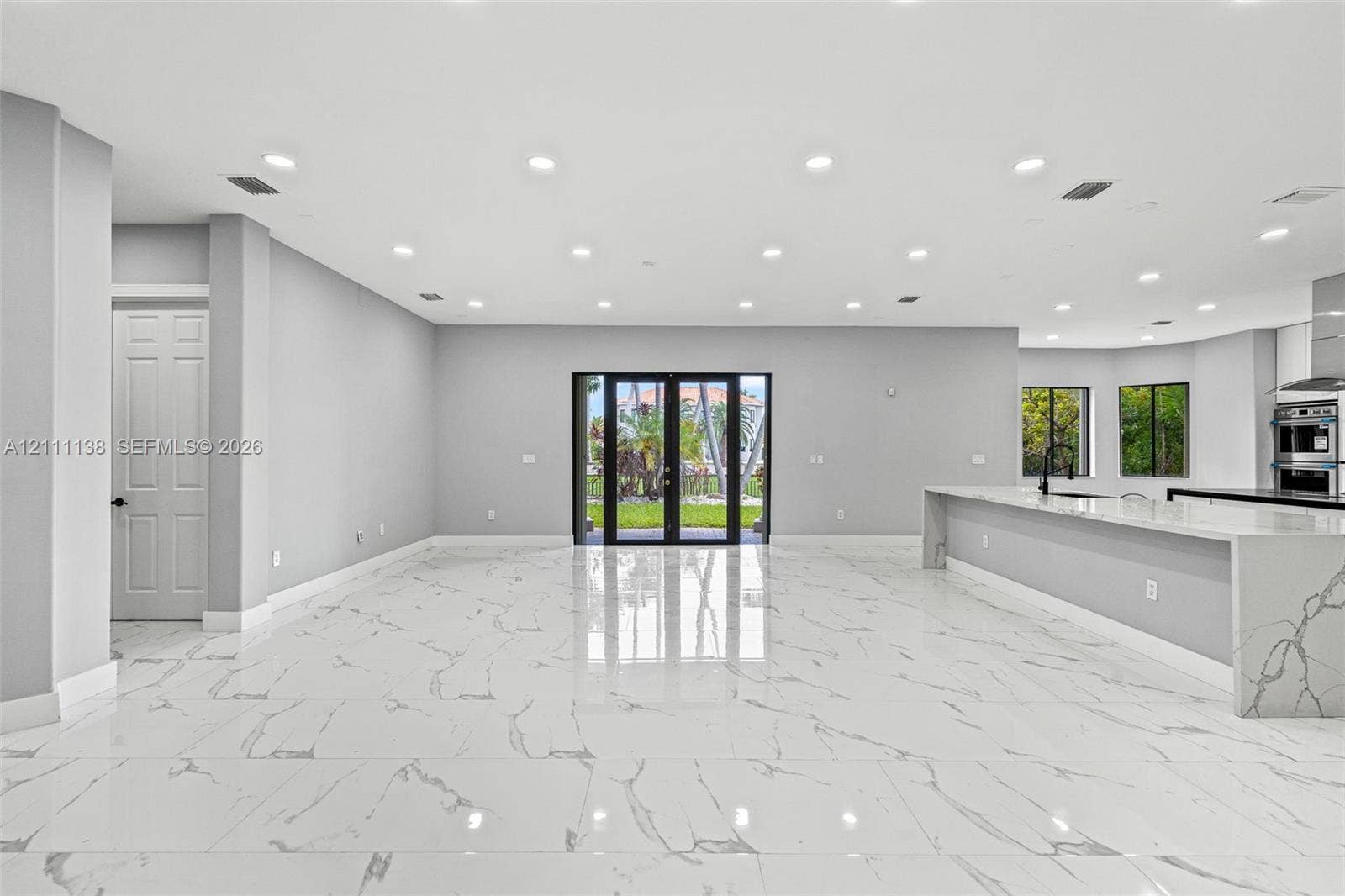 19363 SW 79th Avenue, Cutler Bay, FL 33157 Open-concept interior featuring large-format polished stone flooring, recessed ceiling lighting, a waterfall-edge kitchen island, and double glass-paned doors