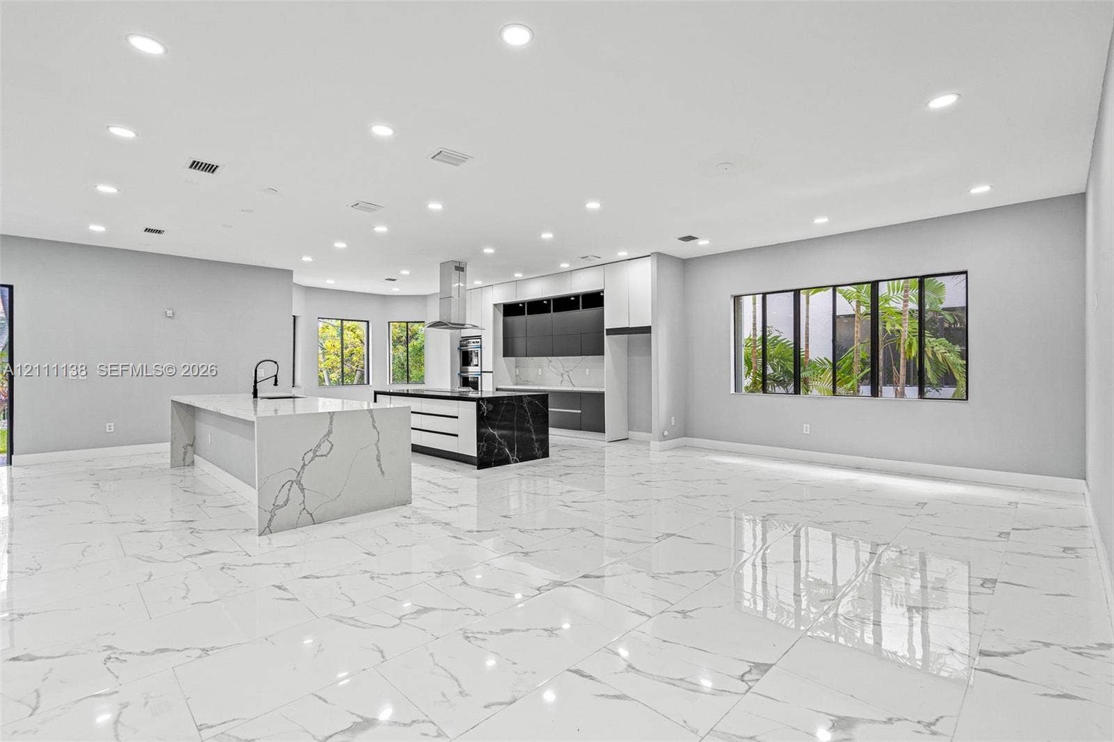 19363 SW 79th Avenue, Cutler Bay, FL 33157 Open-concept kitchen featuring dual islands with veined stone-finish countertops, matte black plumbing fixtures, two-tone flat-panel cabinetry, and polished large-format tile flooring
