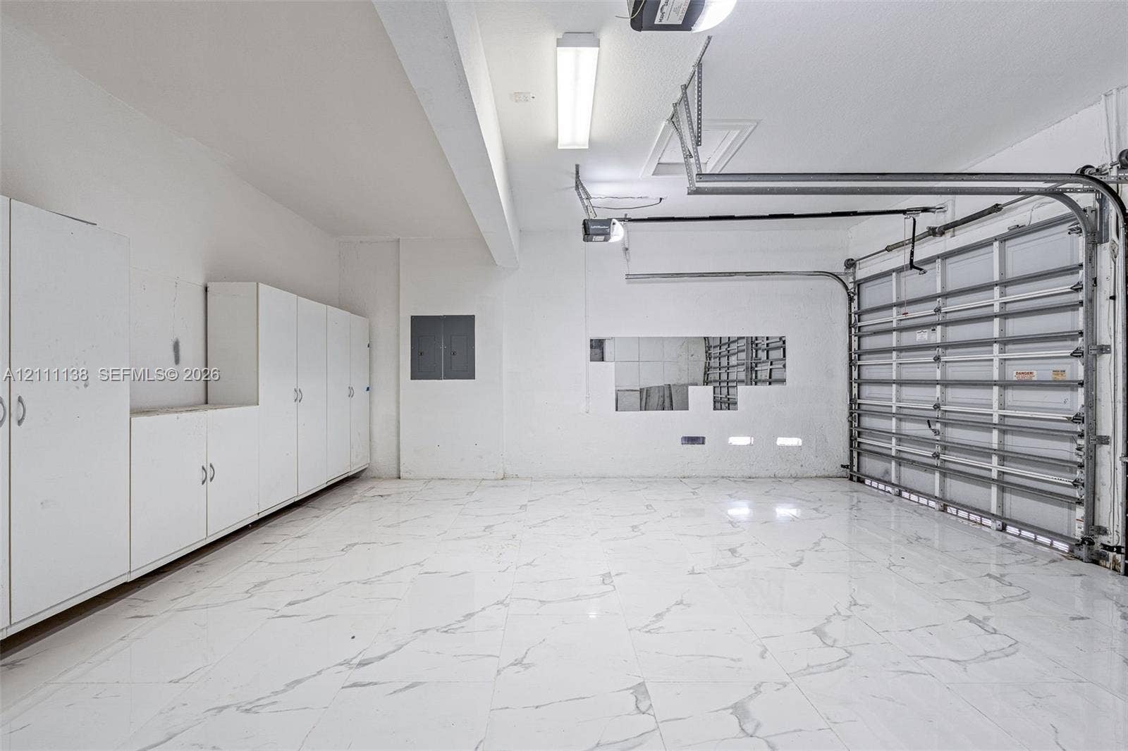 19363 SW 79th Avenue, Cutler Bay, FL 33157 Garage featuring expansive stone-finish flooring, extensive white built-in cabinetry, overhead task lighting, and an automated sectional door