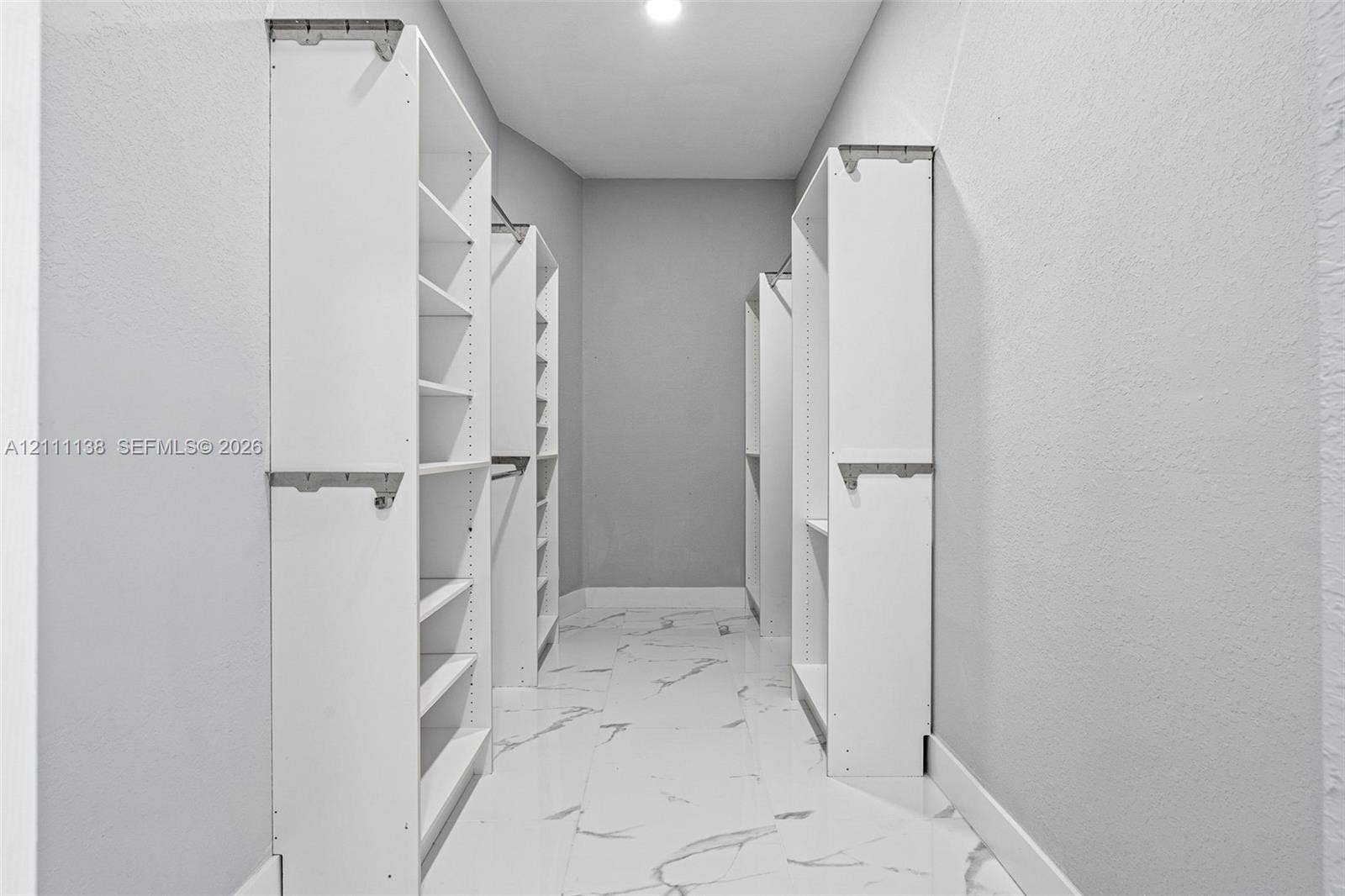 19363 SW 79th Avenue, Cutler Bay, FL 33157 Walk-in closet featuring white built-in shelving, multiple hanging rods, and large-format tile flooring with a neutral vein pattern