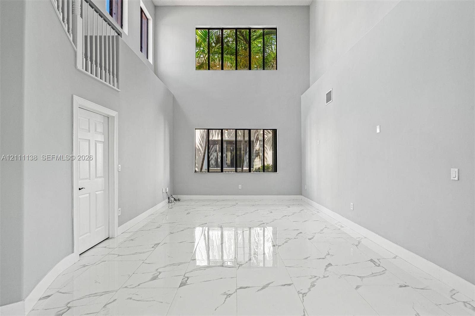 19363 SW 79th Avenue, Cutler Bay, FL 33157 High-ceiling interior featuring polished tile flooring with marble-patterned finish, two tiers of large picture windows, and a white interior railing