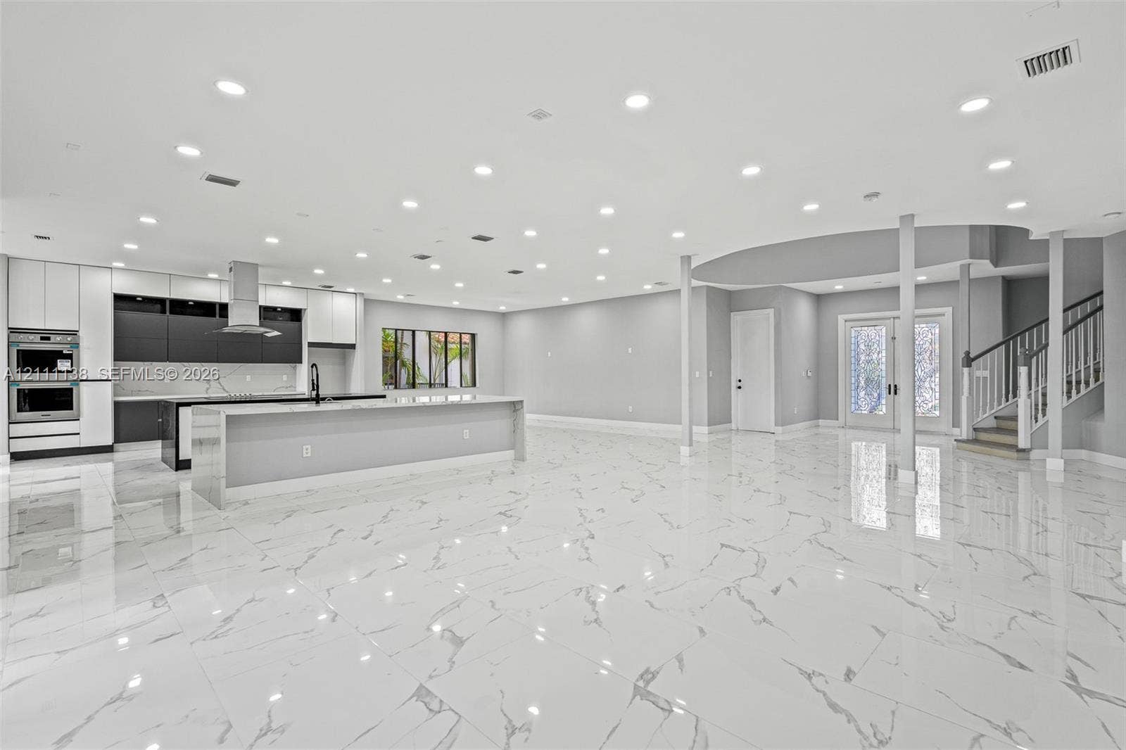 19363 SW 79th Avenue, Cutler Bay, FL 33157 Open-concept interior featuring large-format tile flooring, recessed lighting, a modern kitchen with a dual-tone cabinetry finish, a central island, and a staircase with a wooden handrail