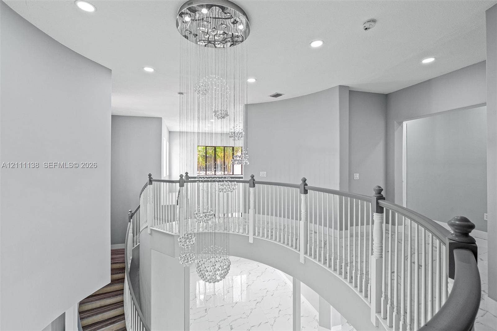 19363 SW 79th Avenue, Cutler Bay, FL 33157 Curved balcony featuring a multi-tiered crystal chandelier, white stone-finish flooring with grey veining, and a white balustrade with a contrasting handrail