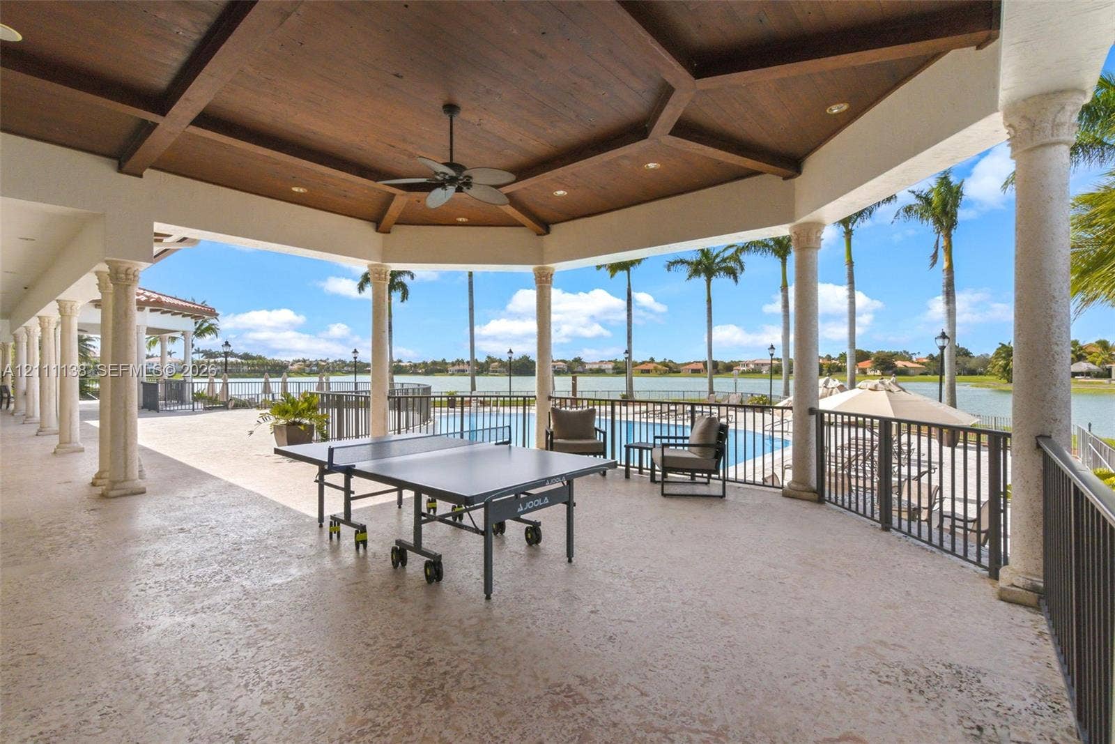 19363 SW 79th Avenue, Cutler Bay, FL 33157 Covered outdoor patio featuring a wood-paneled coffered ceiling, stone-finished flooring, decorative columns, and a metal railing overlooking a pool and waterfront