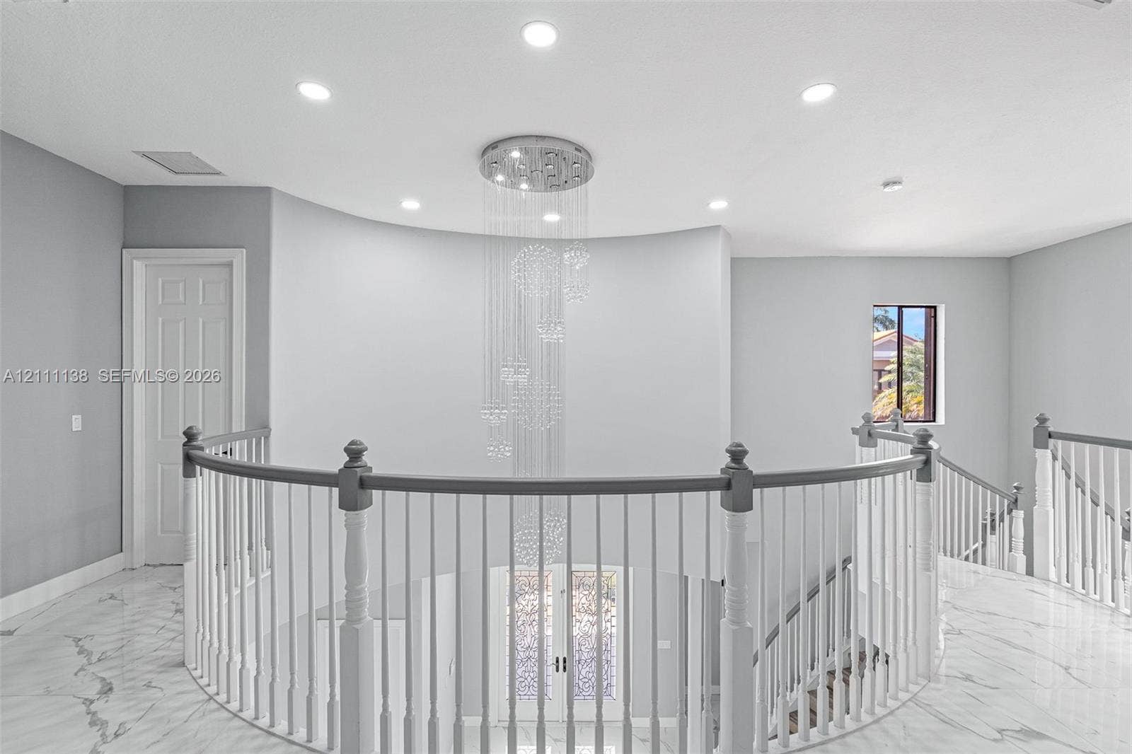 19363 SW 79th Avenue, Cutler Bay, FL 33157 Curved architectural wall featuring a multi-tiered crystal chandelier, polished stone flooring, and a balustrade staircase with wood-finish handrails