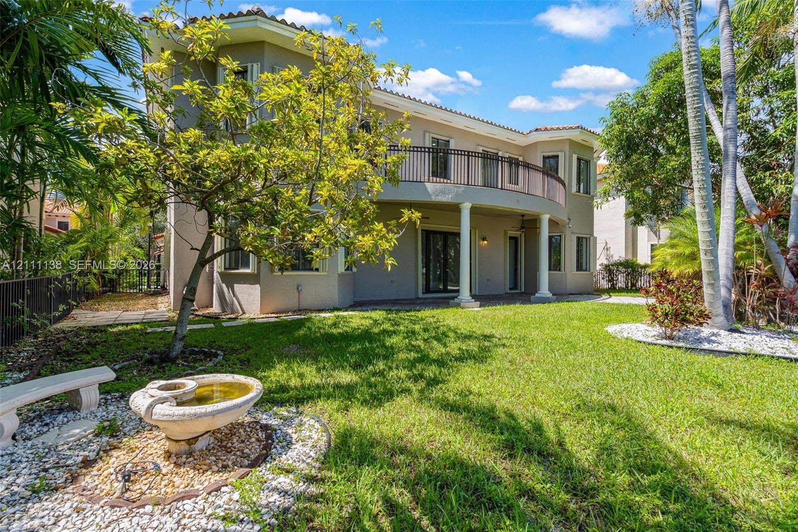 19363 SW 79th Avenue, Cutler Bay, FL 33157 Two-story stucco exterior featuring a curved upper-level balcony with metal railing, classic columns, stone-accented landscaping, and a tiered fountain