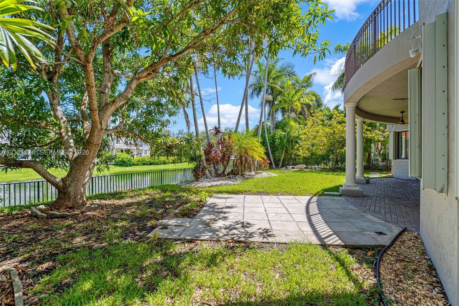 19363 SW 79th Avenue, Cutler Bay, FL 33157 Waterfront backyard featuring a stone paver patio, a covered brick-paved terrace, column supports, and a metal balcony railing