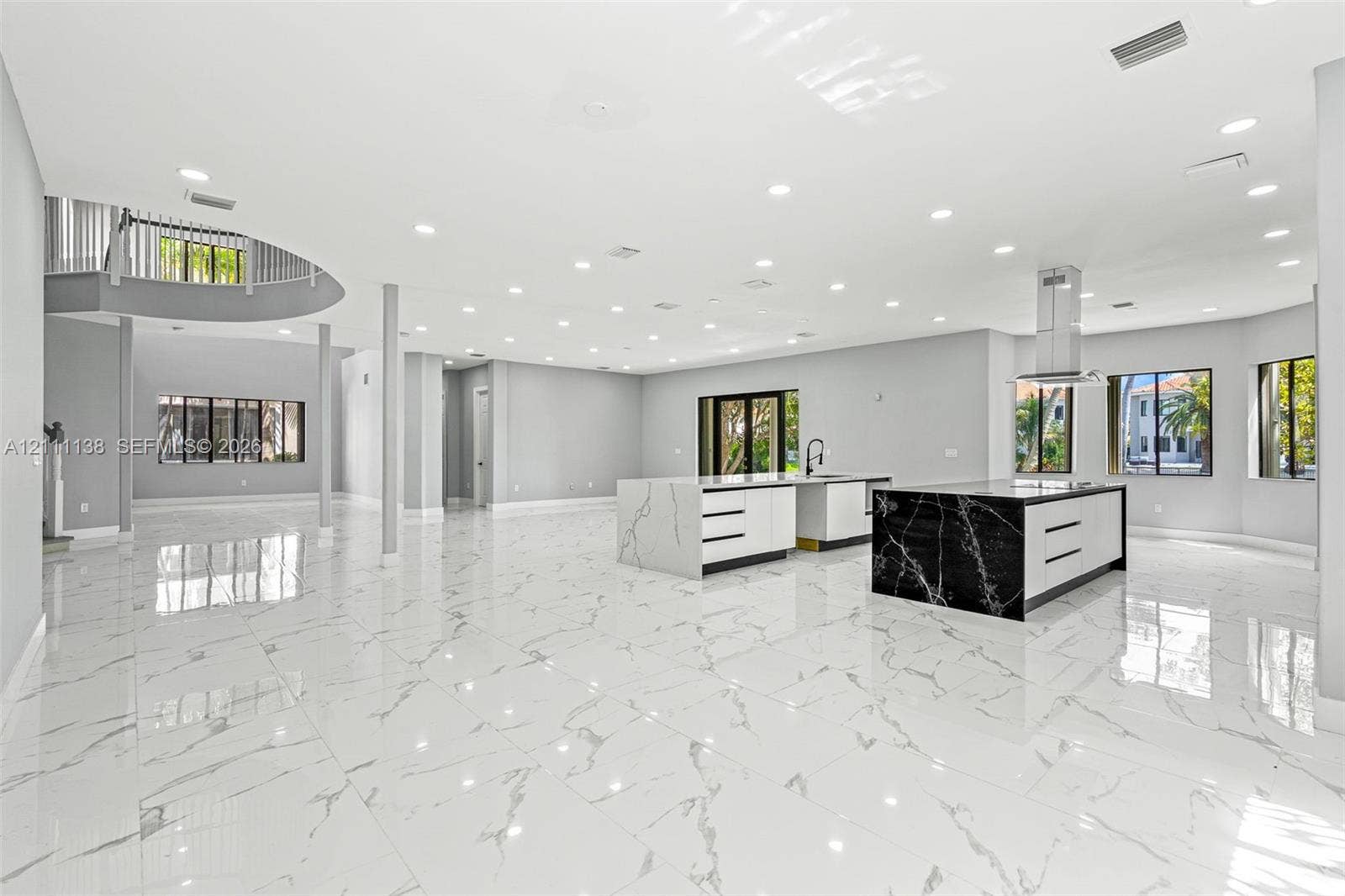 19363 SW 79th Avenue, Cutler Bay, FL 33157 Open-concept living space featuring large-format tile flooring, dual kitchen islands with contrasting waterfall-edge stone surfaces, recessed ceiling lighting, and a curved staircase with a metal balustrade