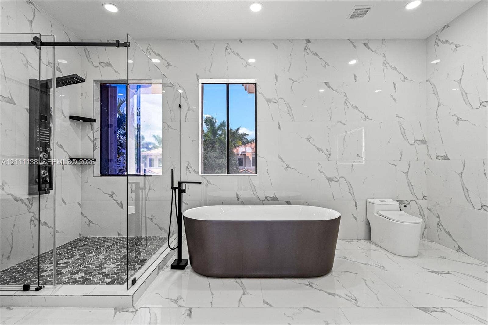 19363 SW 79th Avenue, Cutler Bay, FL 33157 Full-height, large-format stone-patterned wall tile, freestanding soaking tub with floor-mounted matte black faucet, glass-enclosed walk-in shower with matte black rainfall showerhead, and hexagonal mosaic floor tile