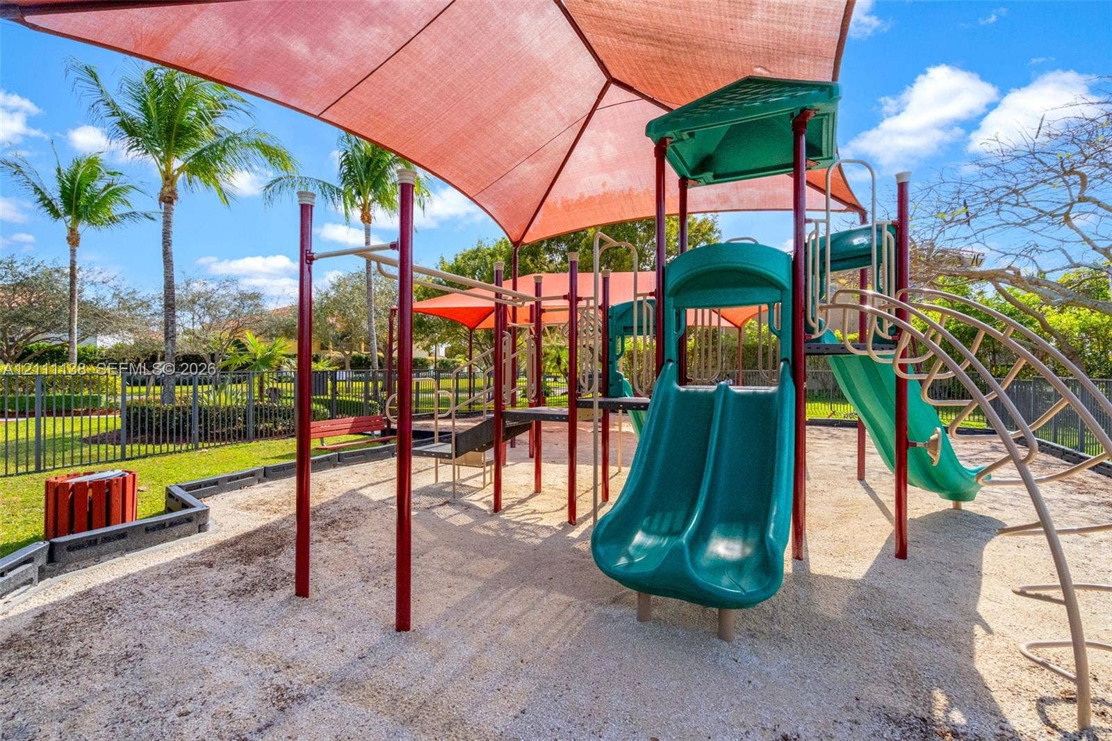 19363 SW 79th Avenue, Cutler Bay, FL 33157 Outdoor recreational area featuring a multi-component play structure with dual slides, suspended shade canopy, rubberized mulch surfacing, and perimeter metal fencing
