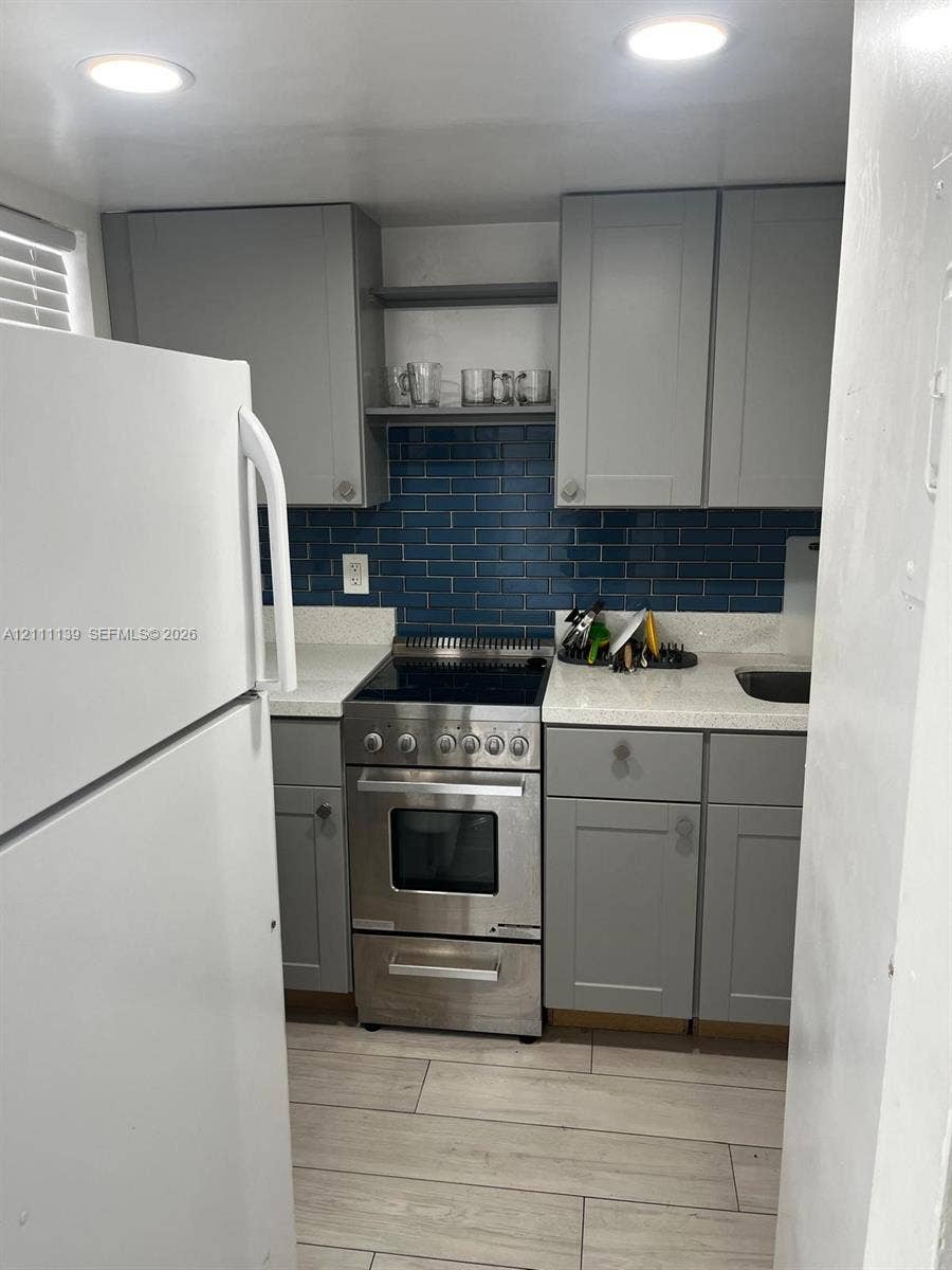 1333 E Hallandale Beach Boulevard, #236, Hallandale Beach, Hallandale Beach, FL 33009 Kitchen featuring gray cabinetry, blue subway tile backsplash, light-toned stone-finish countertops, stainless steel range, and wood-finish flooring