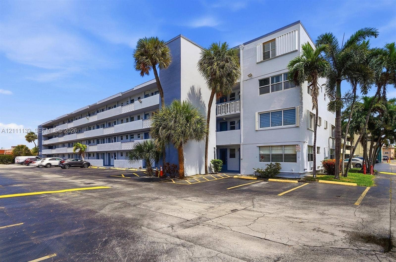 1333 E Hallandale Beach Boulevard, #236, Hallandale Beach, Hallandale Beach, FL 33009 Multi-story building exterior featuring a light-toned stucco facade, tiered exterior walkways, glass windows with horizontal mullions, and mature palm trees