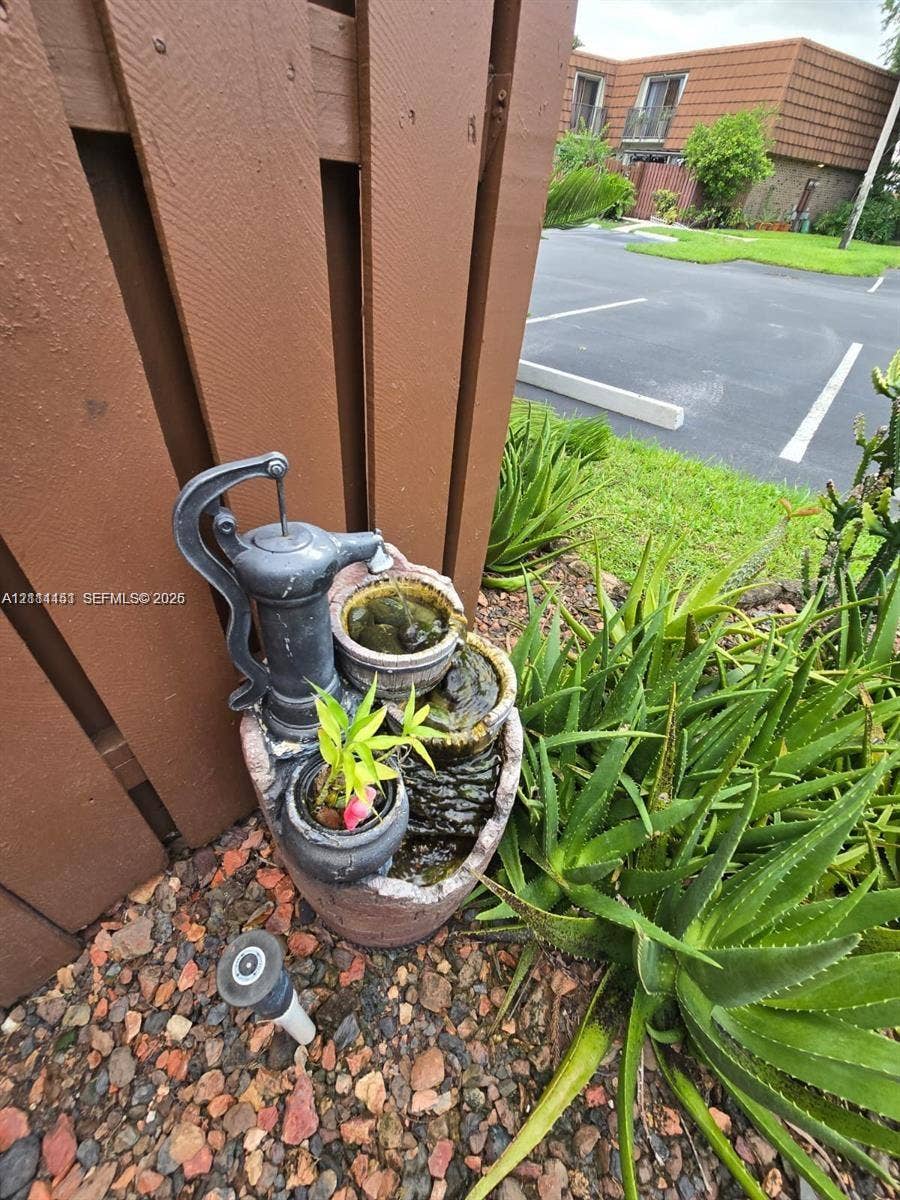Exterior landscape featuring a multi-tiered stone-finish water feature, organic stone ground cover, and aloe vera plantings against a vertical wood-slat fence