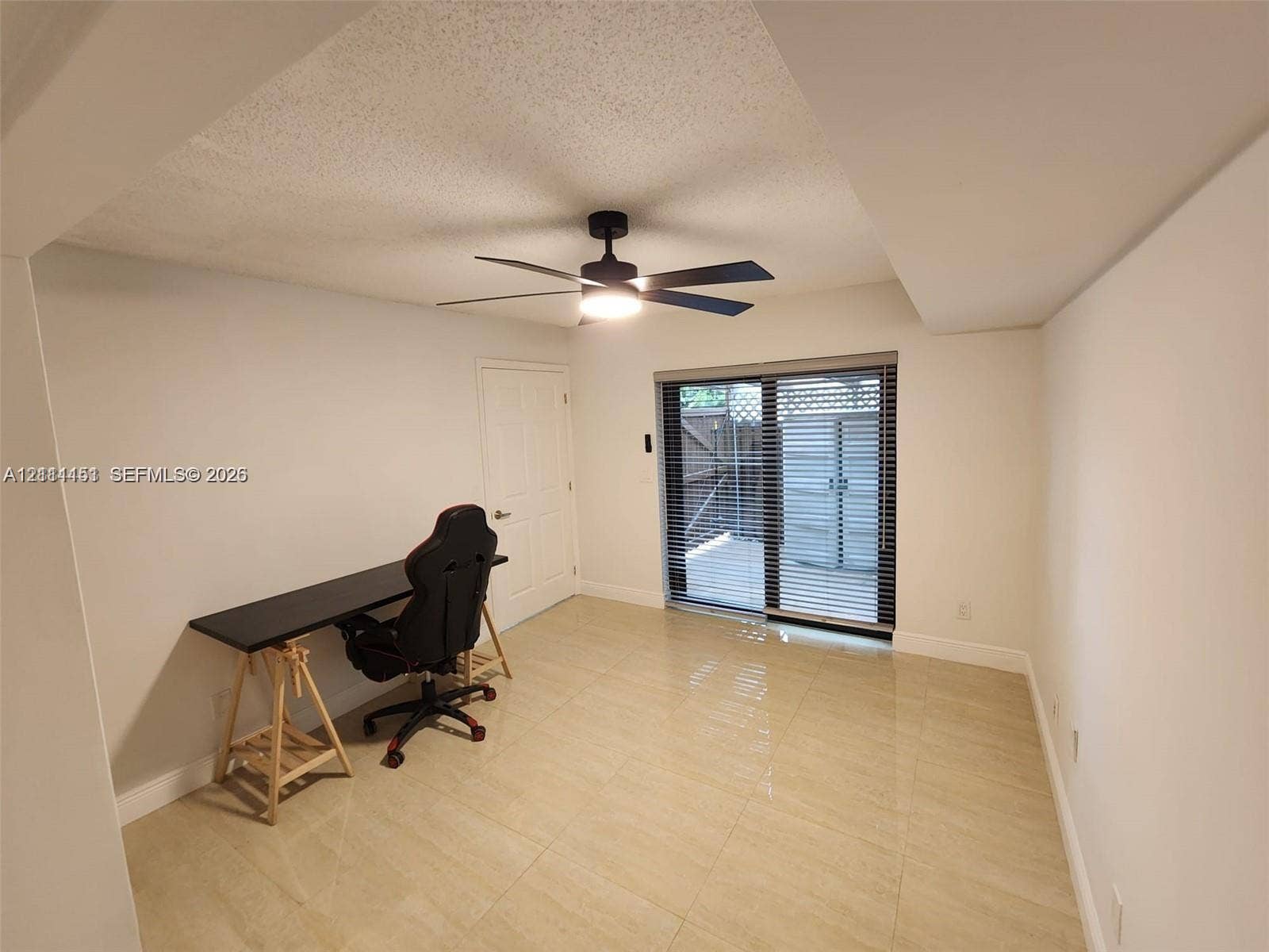Interior space featuring large-format tile flooring, matte black ceiling fan with integrated lighting, and sliding glass doors with window blinds