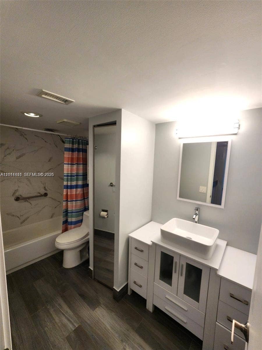 White vanity featuring a rectangular vessel sink and integrated cabinetry, wood-finish flooring, patterned wall tile surround, and an illuminated mirror