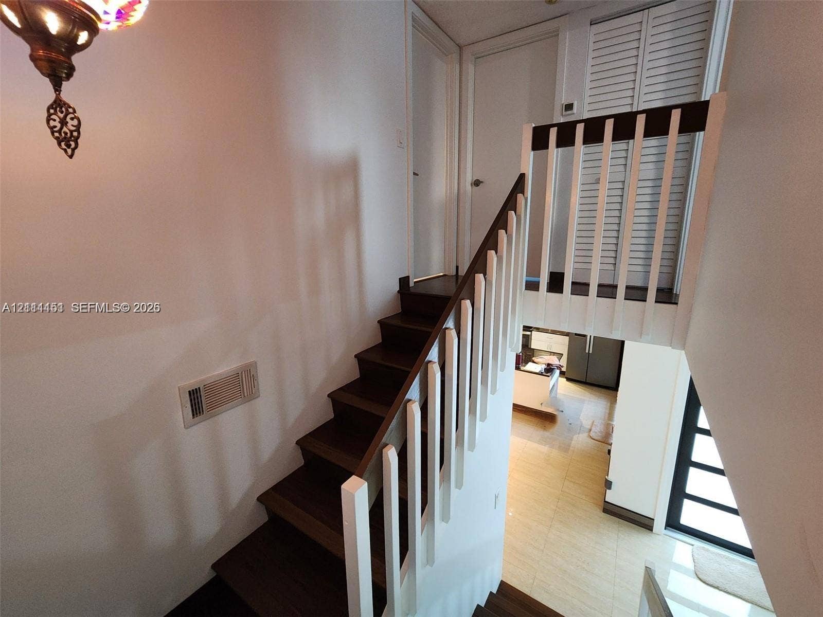Staircase featuring wood-finish treads, white vertical balusters, and a tiered architectural design with louvered closet doors