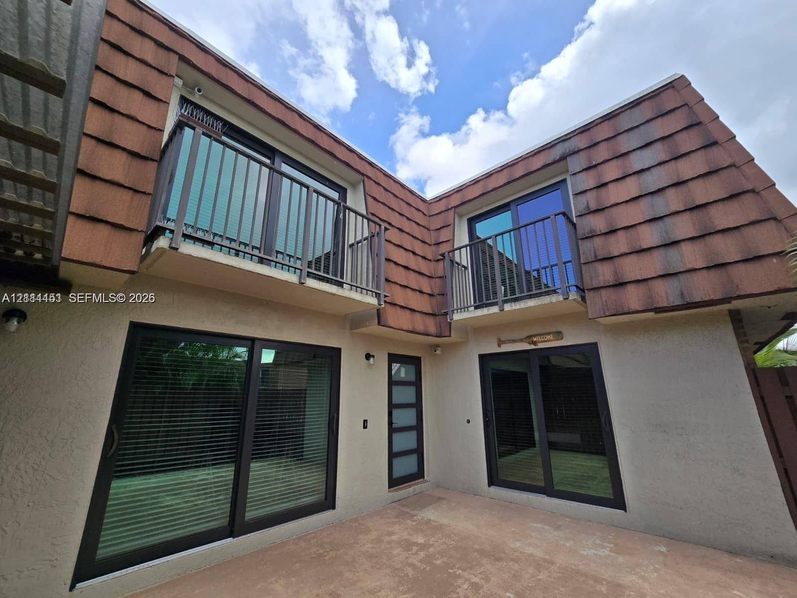 Exterior featuring dual upper-level balconies with metal railings, sliding glass doors with dark frames, a modern entry door with frosted glass panels, and textured shingled roof accents