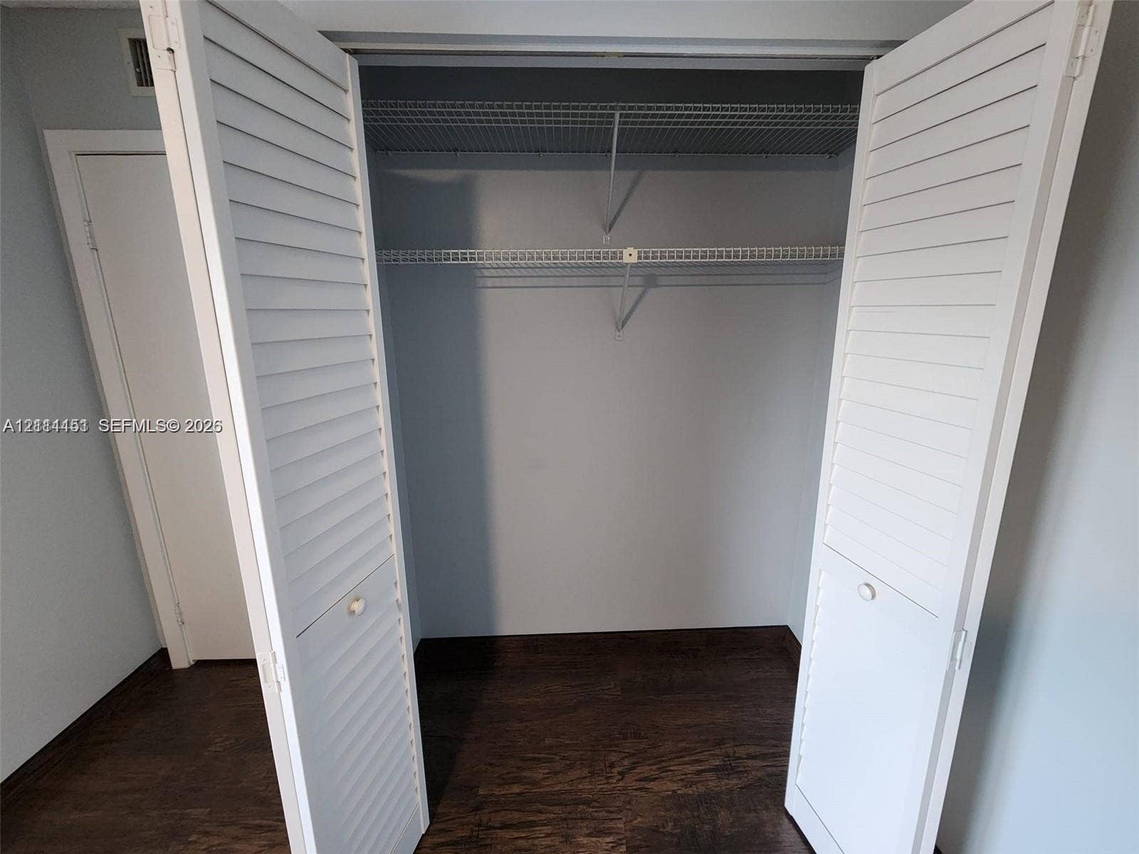 Closet featuring white louvered bi-fold doors, dual white wire shelving, and wood-finish flooring