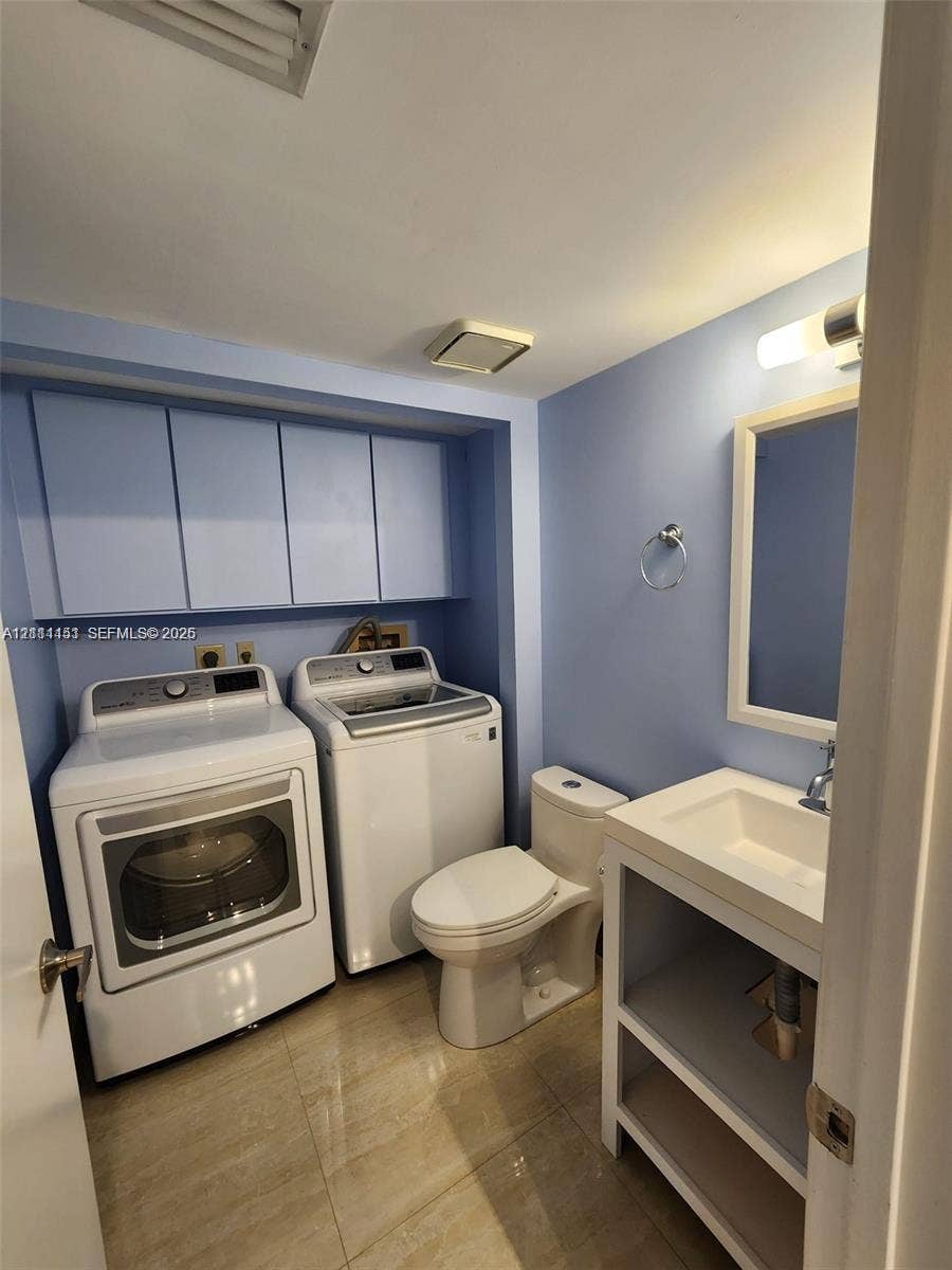 Laundry room featuring built-in overhead cabinetry, a vanity with a rectangular sink, wall-mounted light fixture, and tile flooring