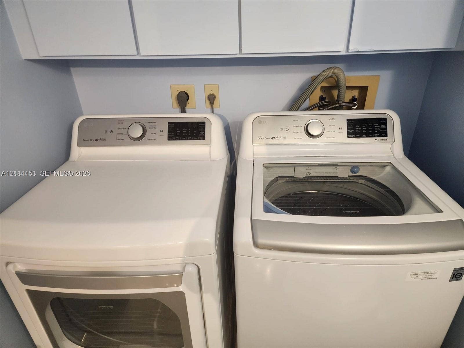 Laundry space featuring white high-capacity top-load washer and front-load dryer with integrated control panels, complemented by overhead white cabinetry