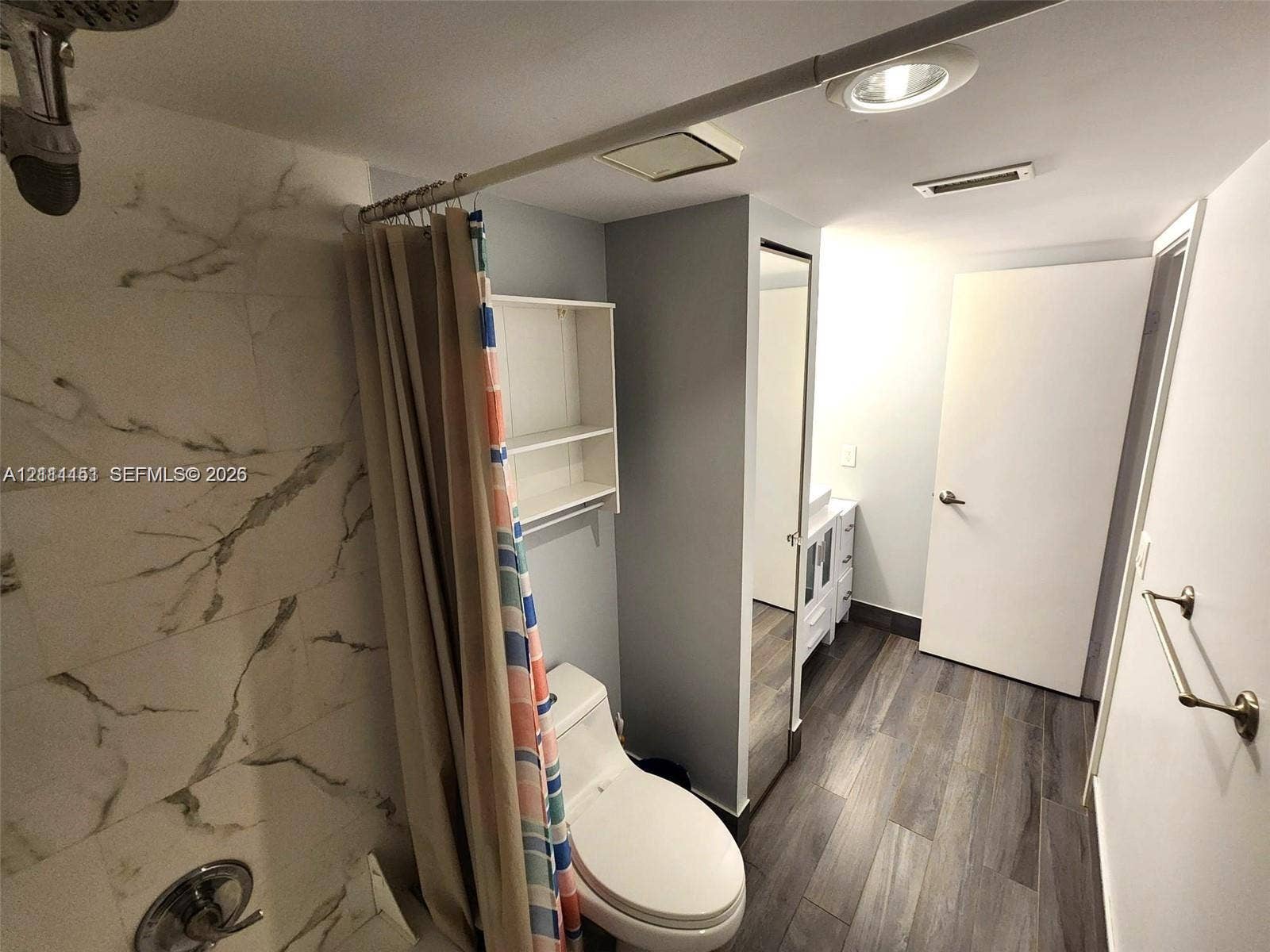 Bathroom featuring shower surround with large-format stone-patterned tile, wood-finish flooring, white vanity, built-in wall shelving, and inset ceiling lighting