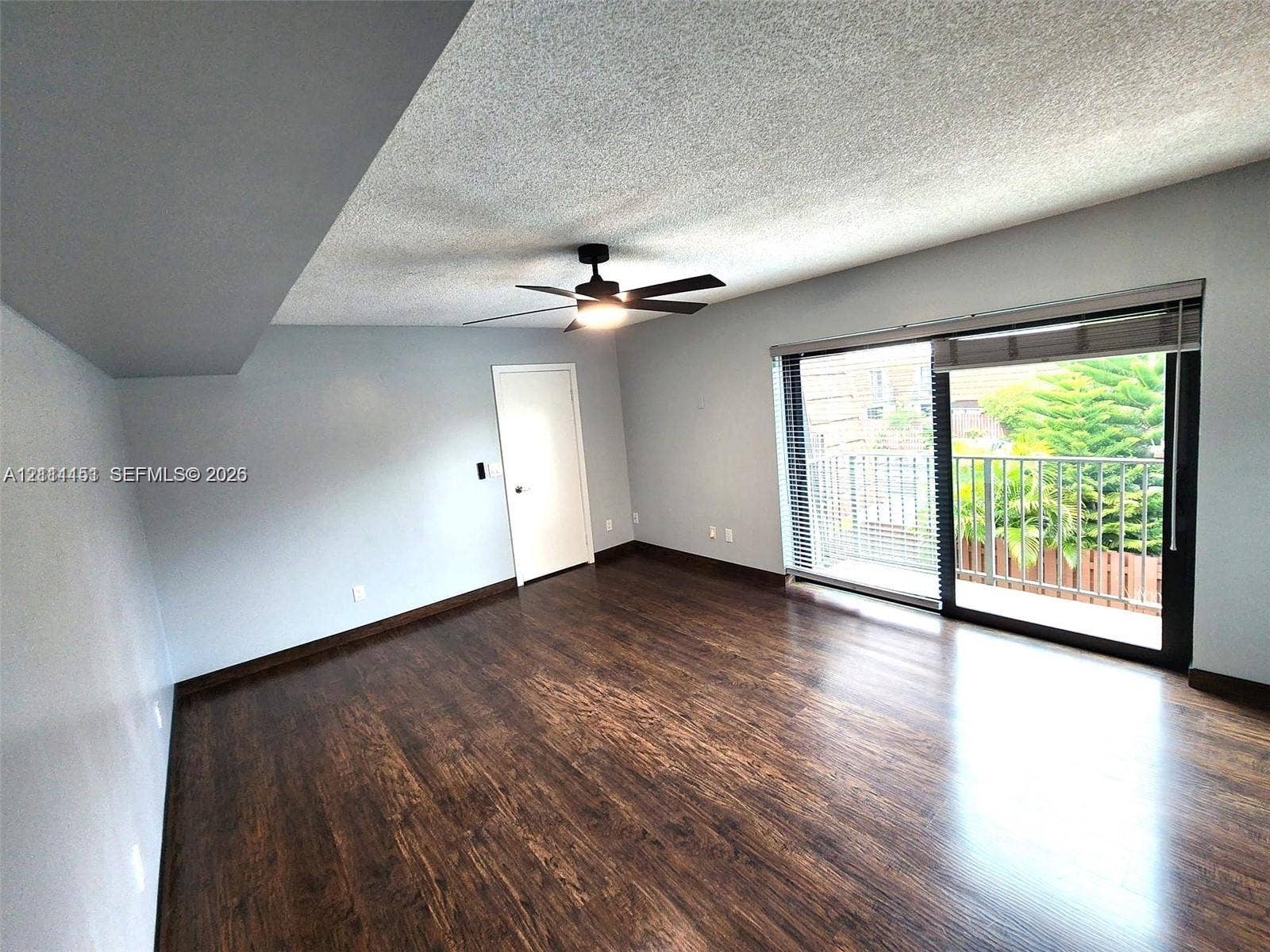 Room featuring wood-finish flooring, a ceiling fan with integrated lighting, and a large sliding glass door opening to an exterior balcony