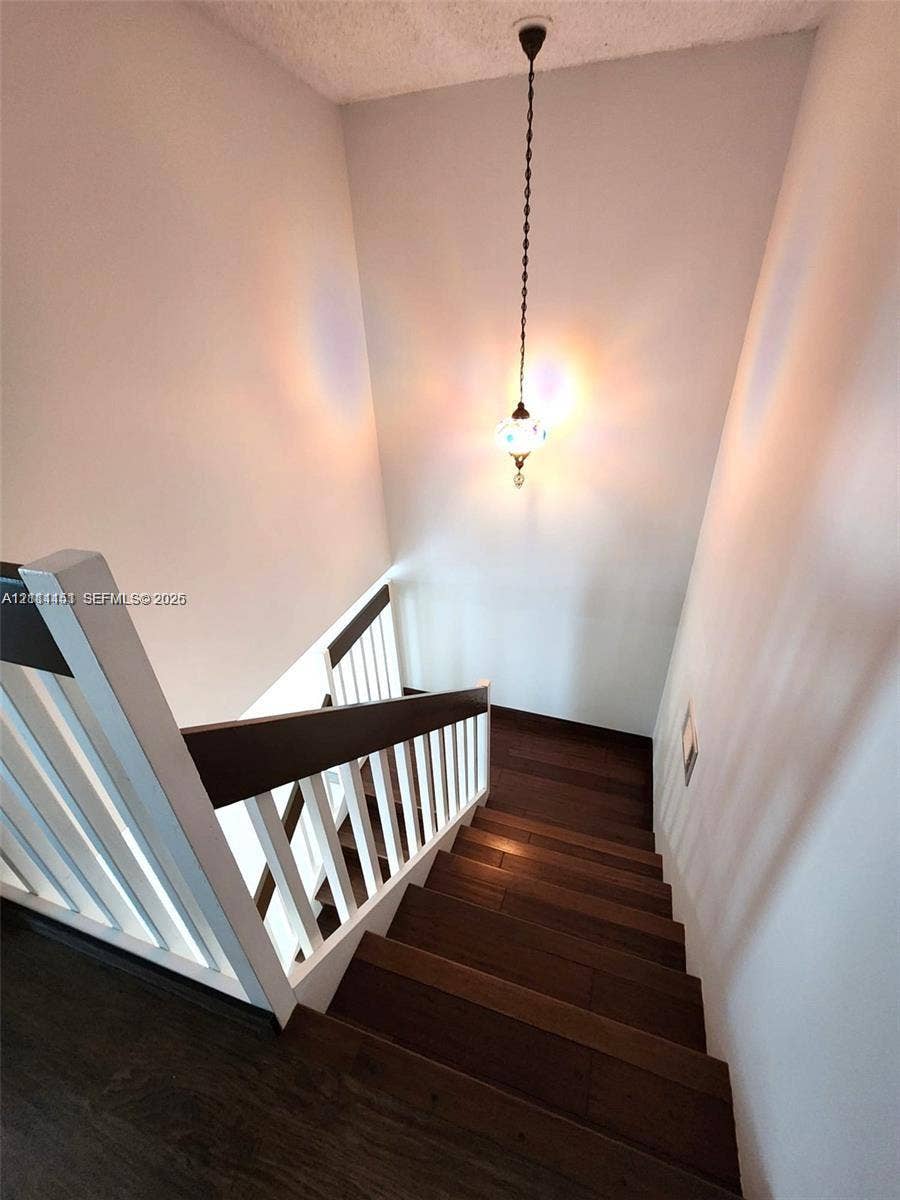 Staircase featuring dark wood-finish treads, a white spindle railing, a dark wood handrail, and a decorative pendant light fixture