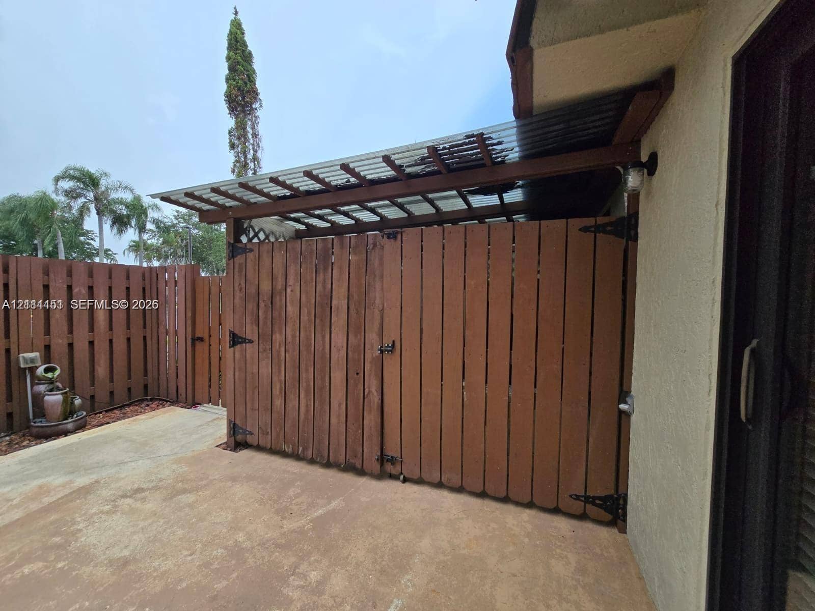 Fenced outdoor storage area featuring vertical wood-plank siding, a corrugated translucent roof covering, and heavy-duty metal hardware