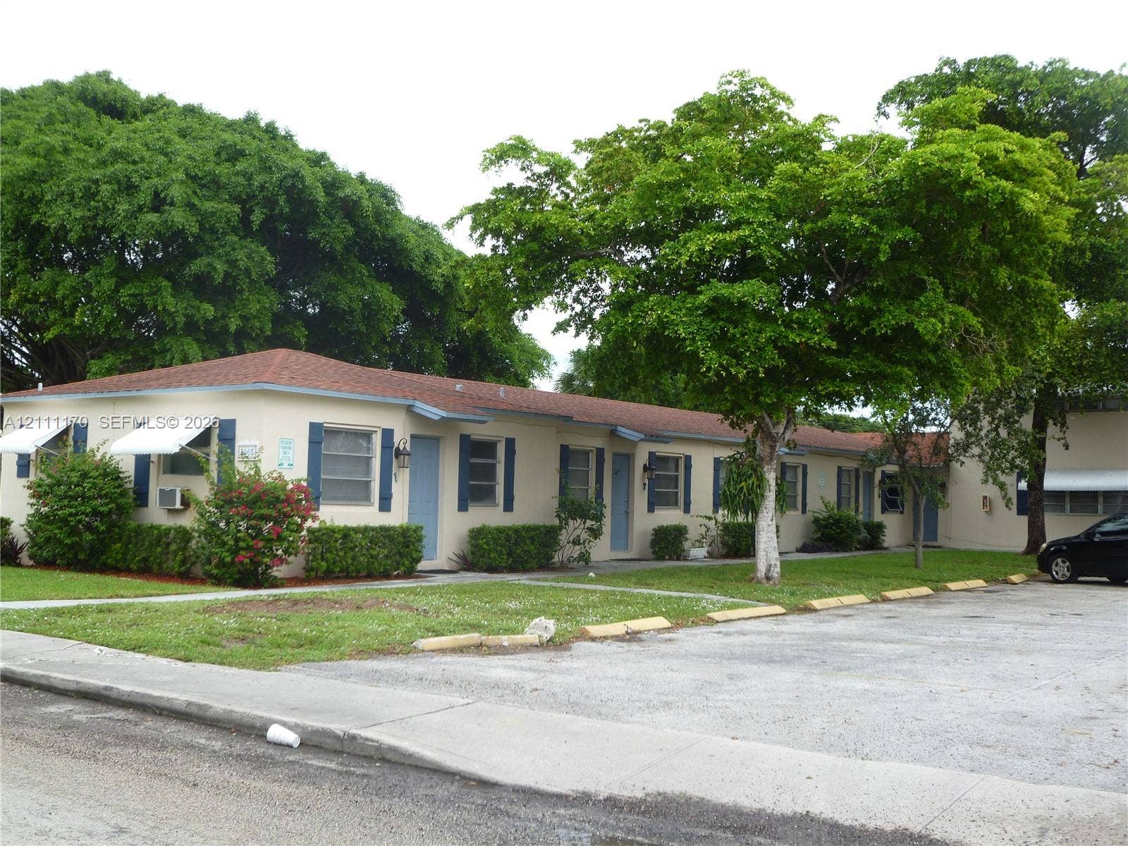 1005 N 18th Court, #5, Hollywood, Hollywood, FL 33020 Single-story exterior featuring a hip roof, blue decorative shutters, assigned surface parking, and mature trees