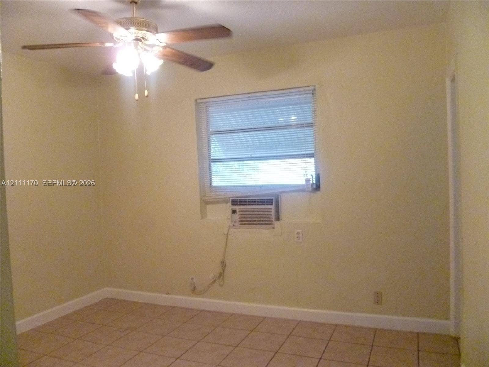 1005 N 18th Court, #5, Hollywood, Hollywood, FL 33020 Interior space featuring ceramic tile flooring, a multi-blade ceiling fan with integrated lighting, a dual-pane window with horizontal blinds, and a built-in wall air conditioning unit
