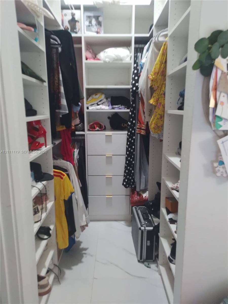 Walk-in closet featuring white custom built-in shelving, four integrated storage drawers, and white tile flooring