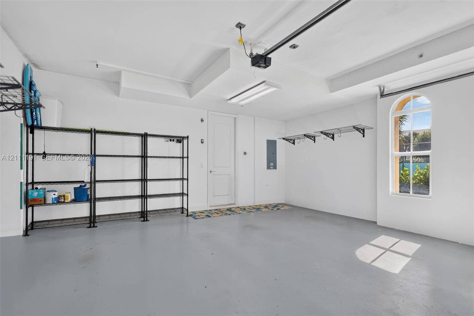 2 car Garage featuring a painted concrete floor, arched window, and overhead fluorescent lighting