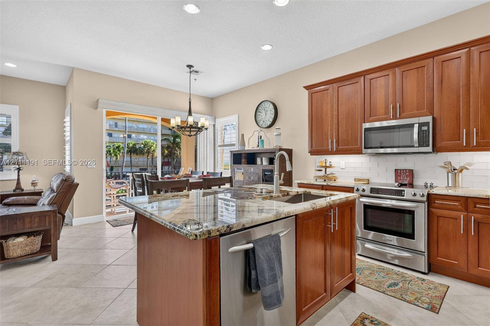 Kitchen featuring wood cabinetry, stone countertops, stainless steel appliances, a center island with an undermount sink, and tile flooring