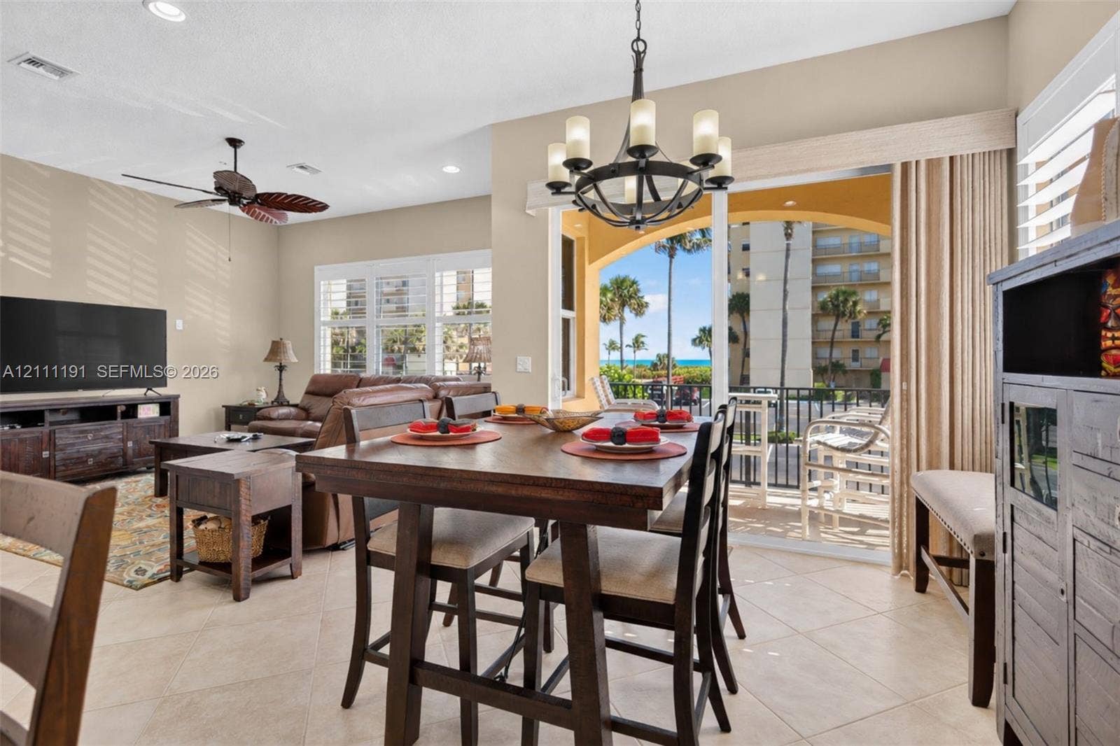 Open-concept living space featuring neutral tile flooring, recessed lighting, a ceiling fan, a multi-arm chandelier, and sliding glass doors opening to a covered balcony