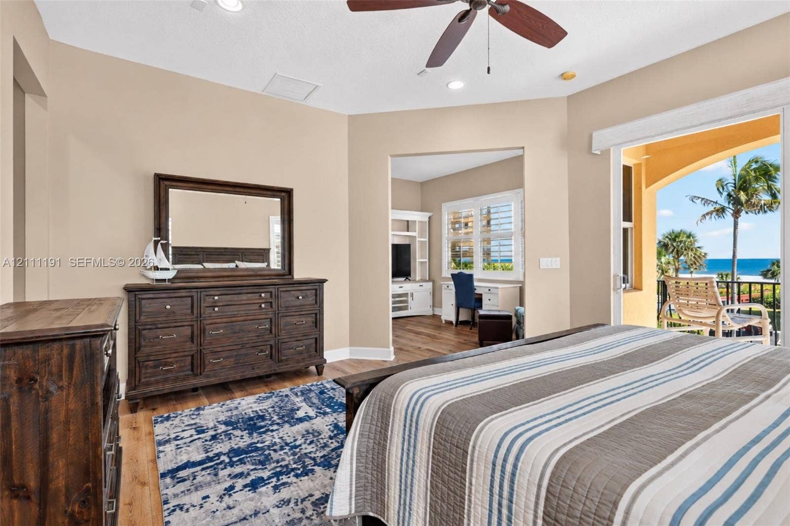 Wood-finish flooring, ceiling fan with light kit, recessed lighting, and sliding glass doors opening to a balcony with an ocean backdrop