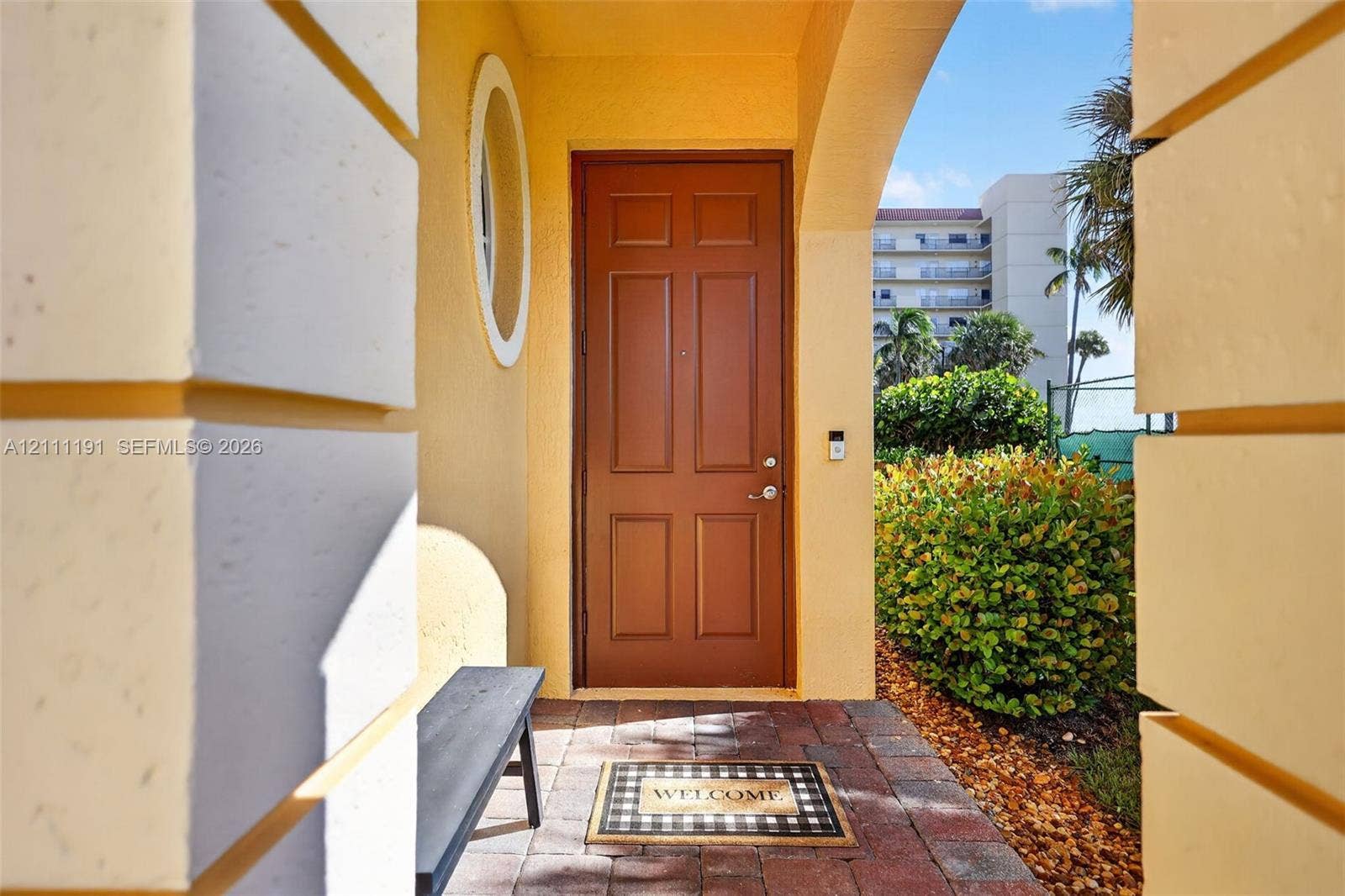 Covered entryway featuring a recessed six-panel door, arched architectural detailing, a circular window, and paver flooring