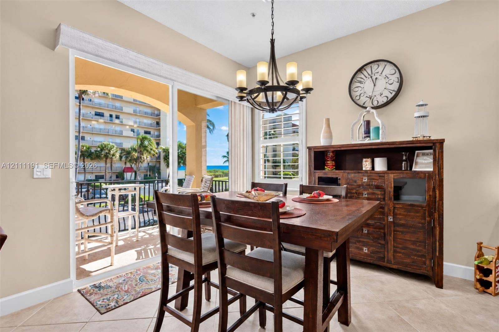 Dining area featuring tile flooring, a multi-arm metal chandelier, plantation shutters, and sliding glass doors opening to a covered balcony with water scenery