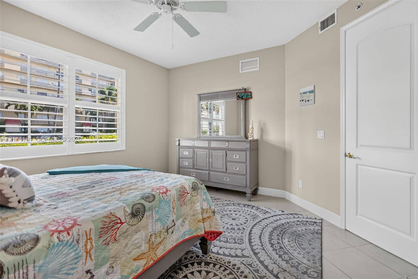 Neutral-toned interior featuring multi-panel shutters, white interior door with arched detail, tile flooring, and a ceiling fan
