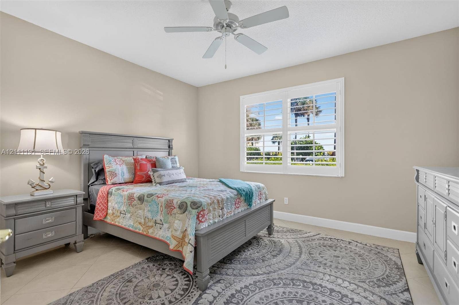 3rd Bedroom on 1st floor. Neutral-toned room featuring a central ceiling fan with light fixture, large plantation shutters, and light-colored tile flooring