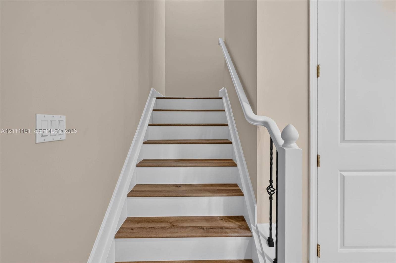 Staircase to the living area featuring wood-finish treads, white painted risers, ornate metal balusters, and a white handrail